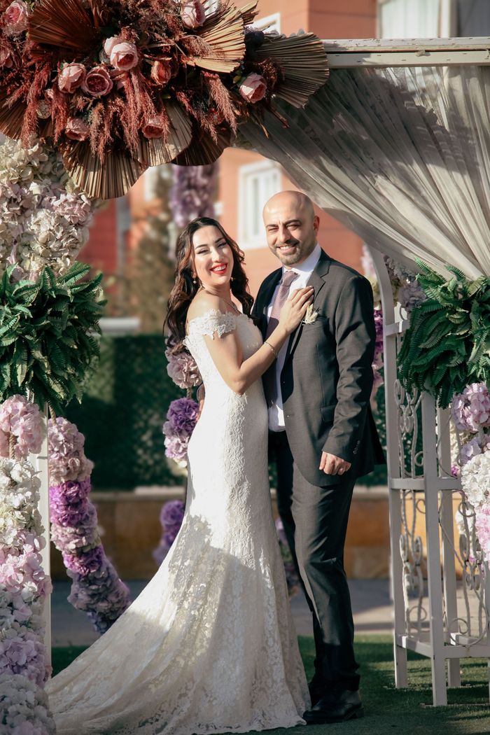 Bride and groom smiling under flower arch on their wedding day.